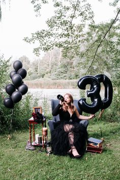 a woman sitting on a chair in the grass with balloons and other items around her