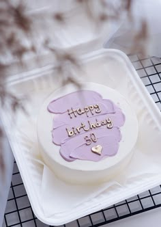 a birthday cake sitting on top of a white tray with purple frosting and gold lettering