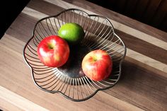 two apples are in a metal bowl on a wooden counter top next to an apple