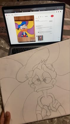 a laptop computer sitting on top of a bed next to a drawing of cartoon characters