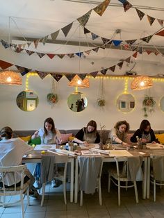 four women sitting at a table with papers and pens in front of them, surrounded by hanging decorations