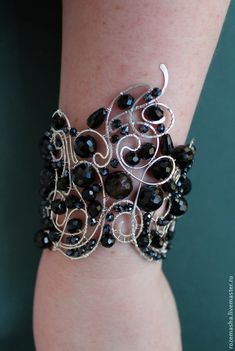 a woman's arm wearing a black and silver bracelet with swirls on it