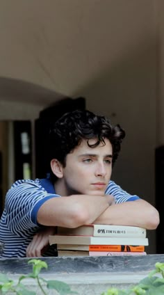 a young man leaning his head on top of two books while looking at the camera