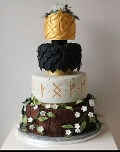 a three tiered cake decorated with black and white frosting, gold crowns and flowers