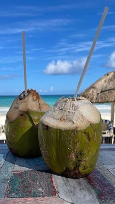 two coconuts sitting next to each other on top of a wooden table near the ocean