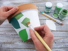 a person is holding a paintbrush and painting leaves on a paper cup with watercolors