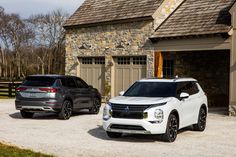 two suvs parked in front of a stone house with brown shingles on the roof