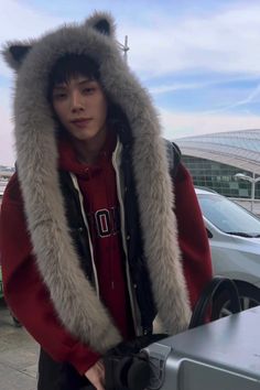 a young man wearing a furry hoodie next to a car