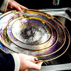 two hands holding plates in front of a sink