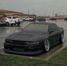 a black car parked in a parking lot next to other cars on a rainy day