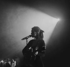 a woman standing in front of a microphone on top of a stage holding a guitar