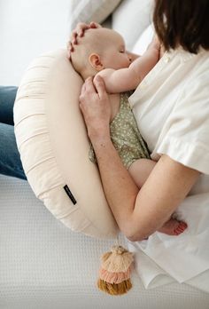 a woman holding a baby in her arms on top of a bed next to pillows