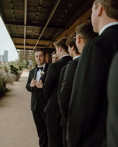 a group of men in tuxedos standing next to each other under a bridge