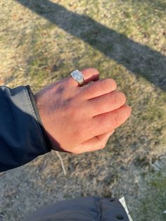 a person wearing a ring on their left hand with grass and dirt in the background