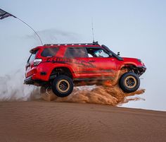 a red four door truck jumping over sand dunes