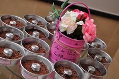 a table topped with lots of tin cans filled with dirt and flowers next to a pink flower pot