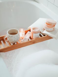 an open book and two cups sit on a bathtub tray next to some candles