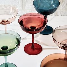 four different colored wine glasses sitting next to each other on a white counter top,