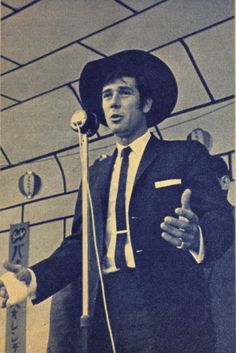 a man in a suit and hat speaking into a microphone