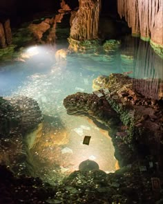 the inside of a cave filled with water and rocks, under a light that is shining on