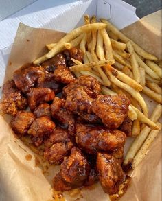 chicken wings and french fries are in a paper container on the table, ready to be eaten