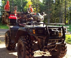 an atv parked on the side of a dirt road in front of trees and grass