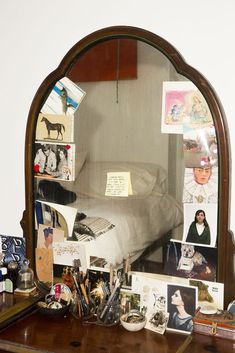 a mirror sitting on top of a wooden dresser filled with pictures and other items next to a bed