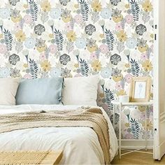 a white bed sitting under a window next to a wallpaper covered in floral designs