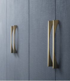 two brass handles are on the side of a blue cabinet with dark gray wallpaper