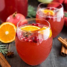 two glasses filled with red wine and garnished with orange slices, cranberries, cinnamon sticks and an apple