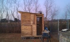 a small wooden outhouse sitting in the middle of a field next to some trees