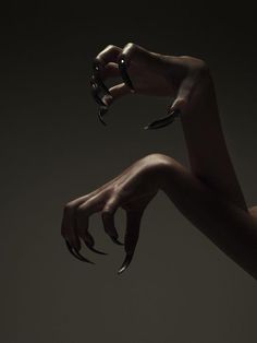 a woman's hands with black nail polish on their nails, holding something in the air