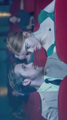 a man and woman sitting next to each other on a red seat in an auditorium