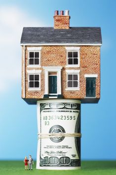 a house on top of a stack of money with two people standing in front of it