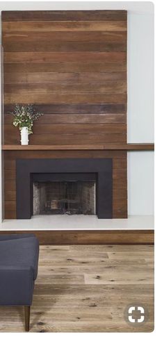 a living room with a fireplace and wooden paneling on the wall above it is a chair