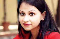 a woman with long black hair wearing a red shirt and looking at the camera while sitting down