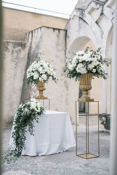 two gold vases with white flowers are on a table in front of an archway