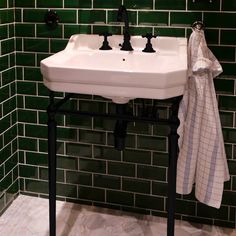 a white sink sitting under a bathroom mirror next to a green tiled wall with black faucet