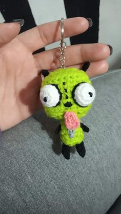 a hand holding a small keychain with a green creature on it