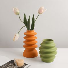 two vases with flowers in them on a table next to a cell phone and candle holder