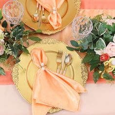 the table is set with gold plates, silverware and peach napkins on it