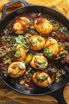 an iron skillet filled with cooked scallops covered in sauce and garnished with fresh herbs