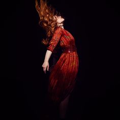 a woman in a red dress with her hair blowing in the wind, on a black background