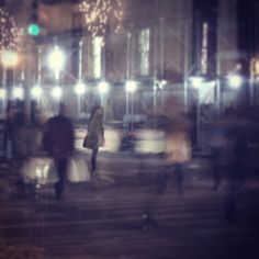 blurry image of people walking down the street at night with lights on and one person carrying luggage