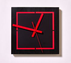 a square clock with red hands on a white wall and black frame in the middle