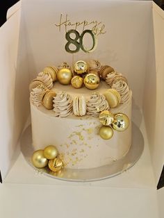 a birthday cake in a box with gold ornaments on it and the number 80 on top