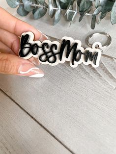 a hand holding a keychain with the word boss mom written in black on it