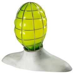 a yellow ball with wire wrapped around it on a white tableclothed surface in front of a gray background