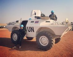 a man standing next to a white armored vehicle in the desert with two men sitting on it