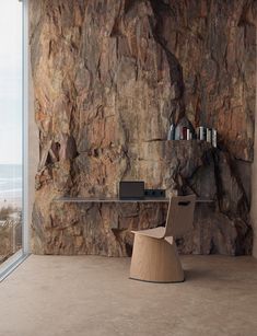 a chair sitting in front of a stone wall next to a book shelf with books on it